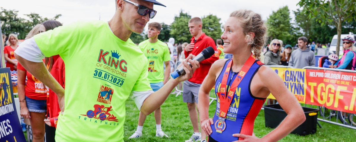 Dr Shannon in bright green shirt interviewing a runner in a blue and red outfit at an outdoor event.