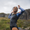 Person in long sleeve swimsuit standing wet with hands raised, natural rocky background