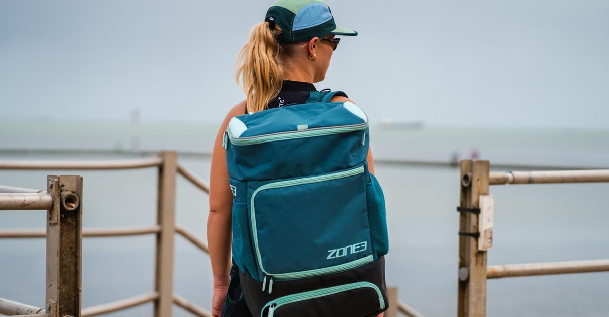 Person wearing a teal Zone3 Award Winning Transition Backpack bag by a body of water.