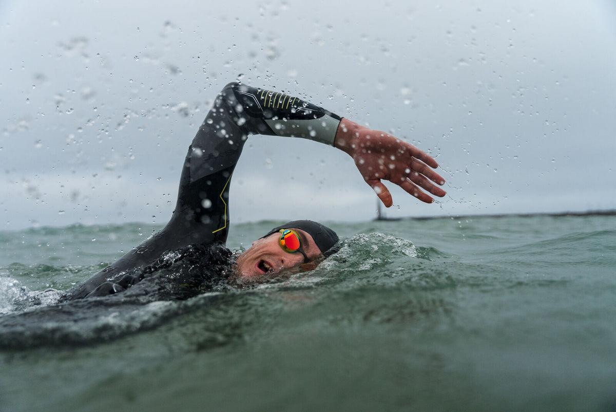 Person swimming in cold water wearing a wetsuit and swim cap.