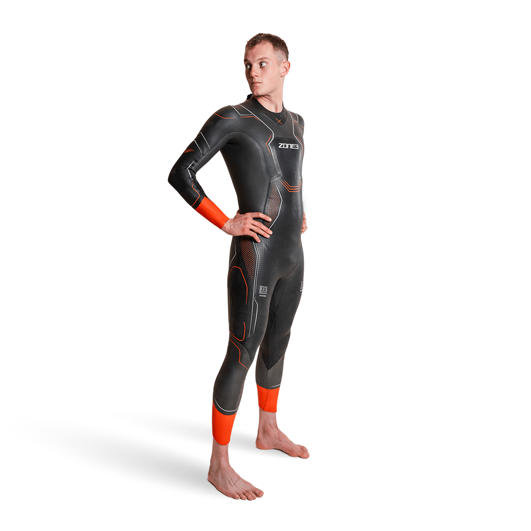 side view of a man wearing the Zone3 Vanquish-X wetsuit with orange accents on white background. 