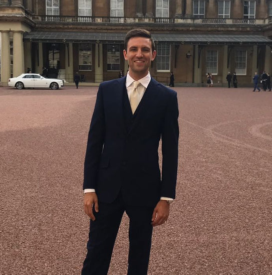 The ZONE3 founder in a suit, standing in the forecourt of Buckingham Palace.
